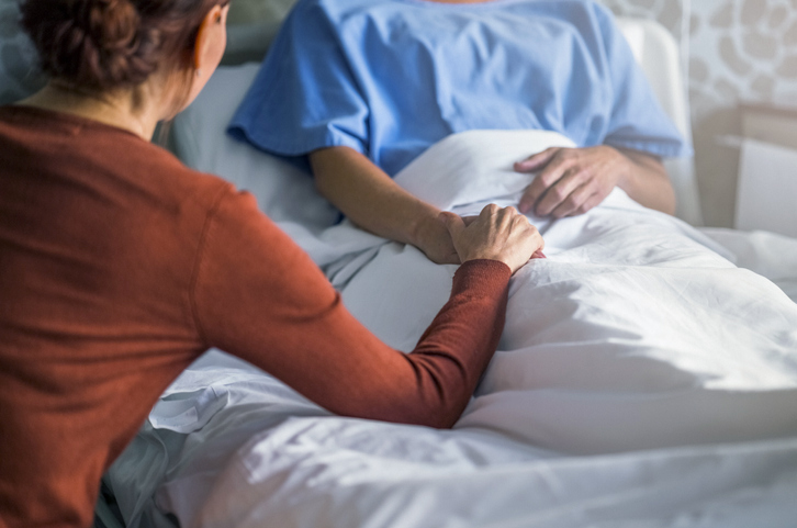 junge Frau hält die Hand einer Frau, die im Krankenbett liegt